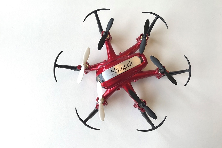 Auf dem Bild sieht man eine rote Drohne mit sechs Rotoren. Auf der Drohne ist ein silbernes Metallschild befestigt, auf welchem bbf.tg.ch zu lesen ist. 