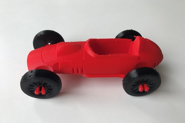Man sieht einen roten, 3D-gedruckten Ferrari ähnlichen Wagen mit schwarzen Rädern.