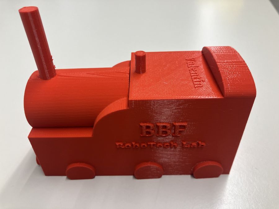 Auf dem Bild ist ein rote Lokomotive zu sehen, die mit dem 3D-Drucker ausgedruckt wurde.