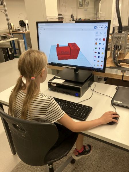 Auf dem Bild ist ein M&auml;dchen am Computer zu sehen, welches eine rote Lokomotive in einem 3D-CAD-Programm konstruiert hat.
