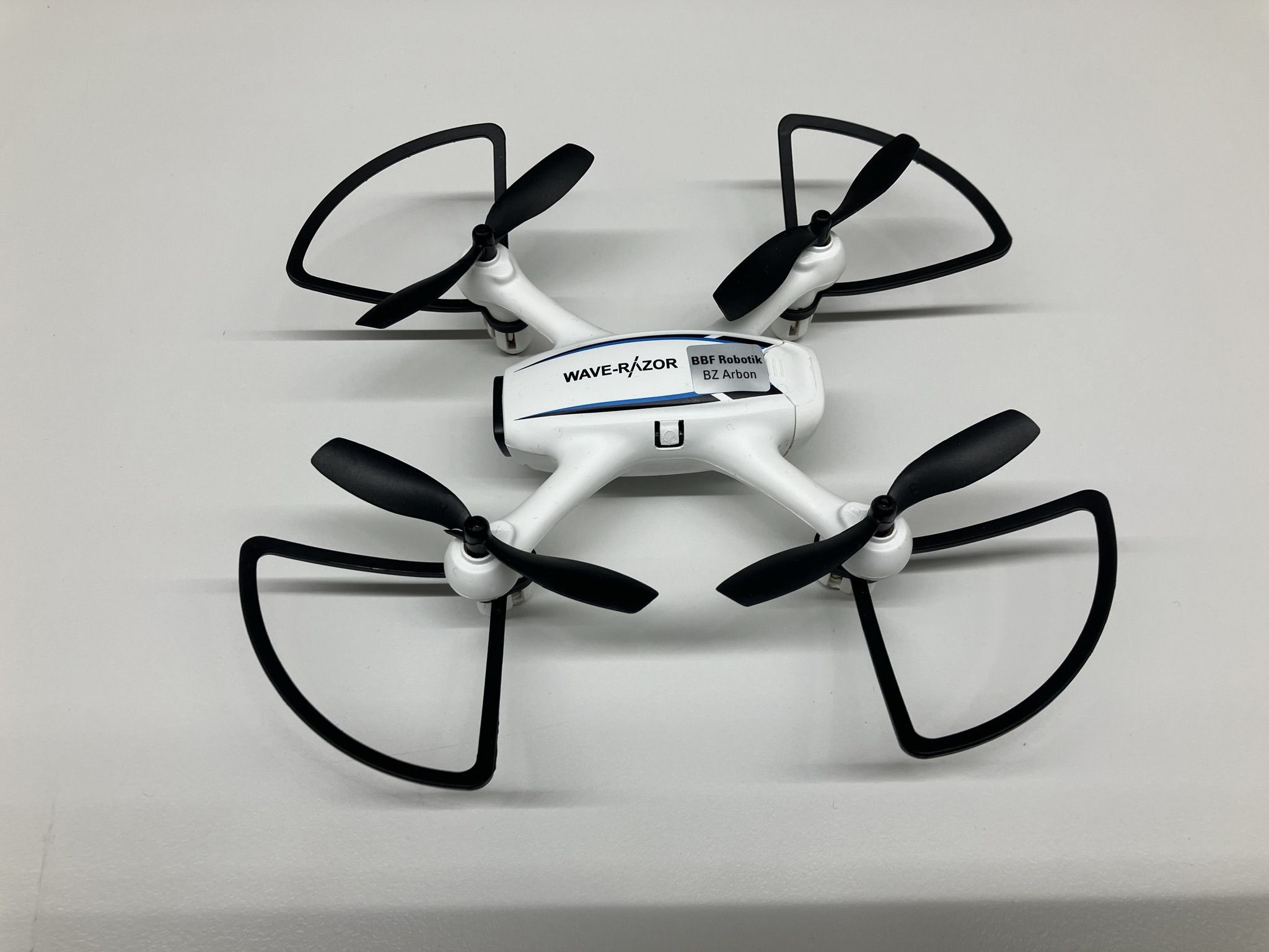 Man sieht eine moderne weisse Drohne mit vier schwarzen Rotoren. Die Drohne wurde von den Industrierobotern montiert.